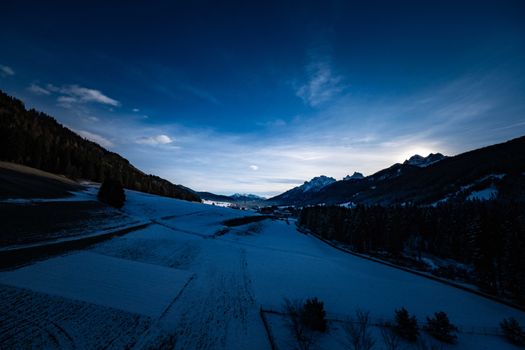 Serene winter sunrise over a snow-covered rural field with mountains in the background.