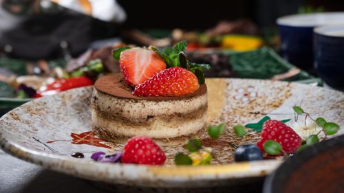 Free Close-up of a tiramisu dessert garnished with strawberries and mint on a decorative plate. Stock Photo