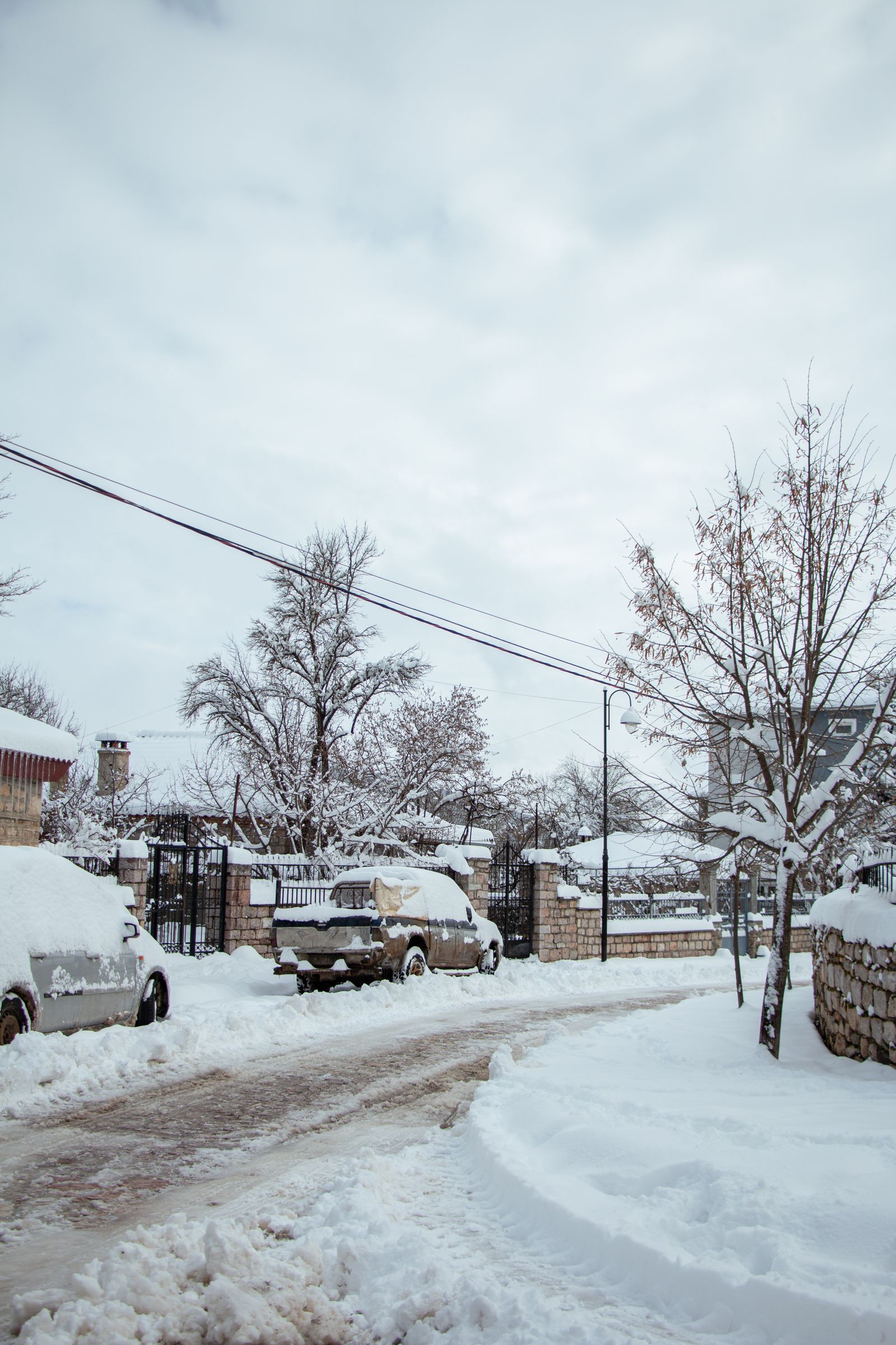 Snow-covered street with bare trees and stone walls in Voskopojë, near Korçë, Albania