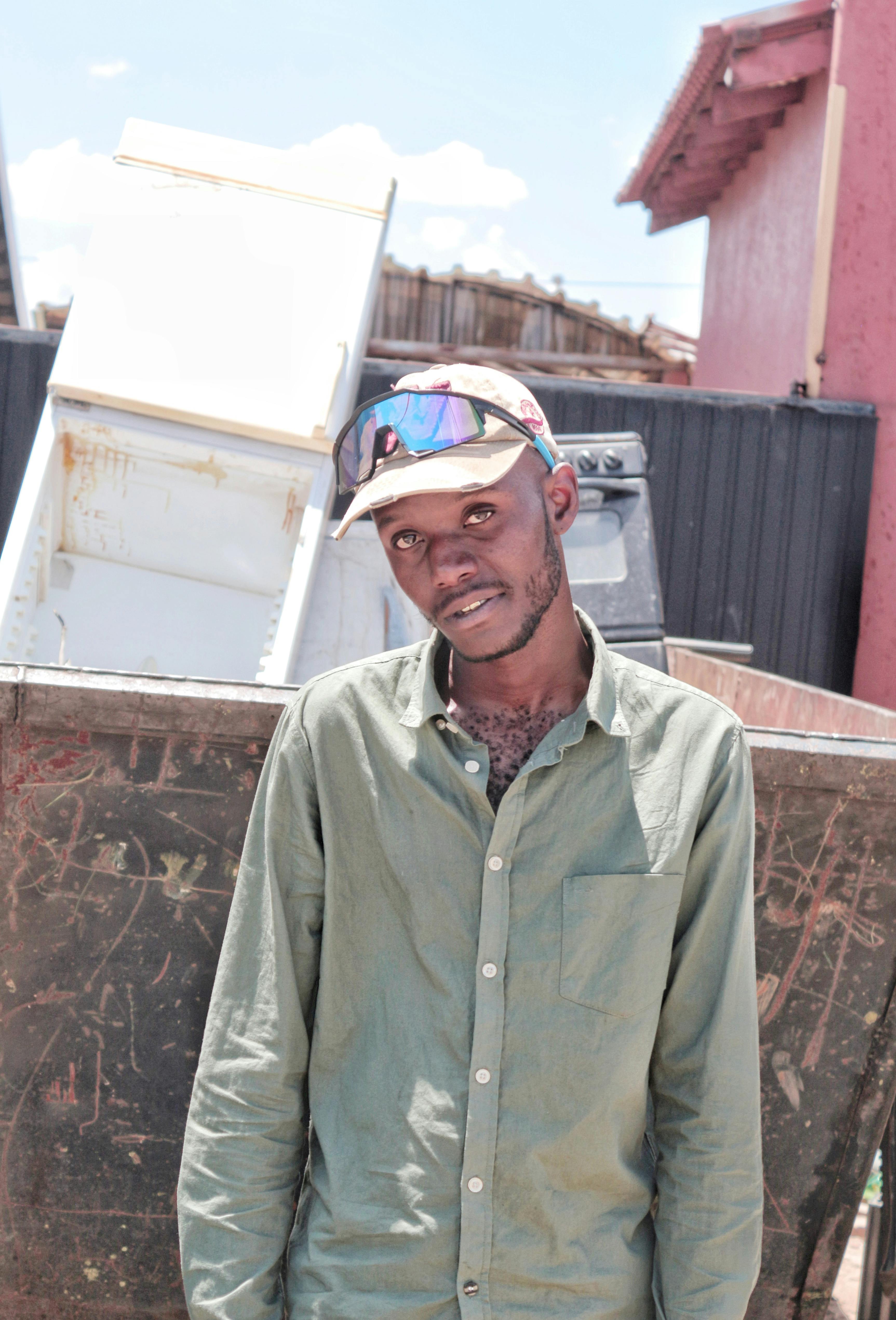 Portrait of an African American man outdoors with casual attire and cap, standing in front of an urban backdrop.