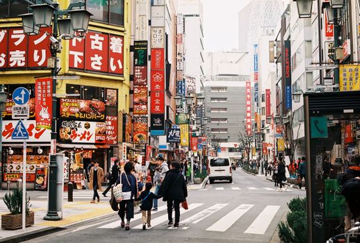 A vibrant street scene in Tokyo featuring crowds, colorful signage, and urban architecture.