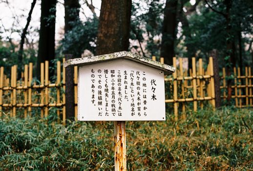 Traditional wooden sign in a Tokyo park surrounded by bamboo fencing and lush trees.
