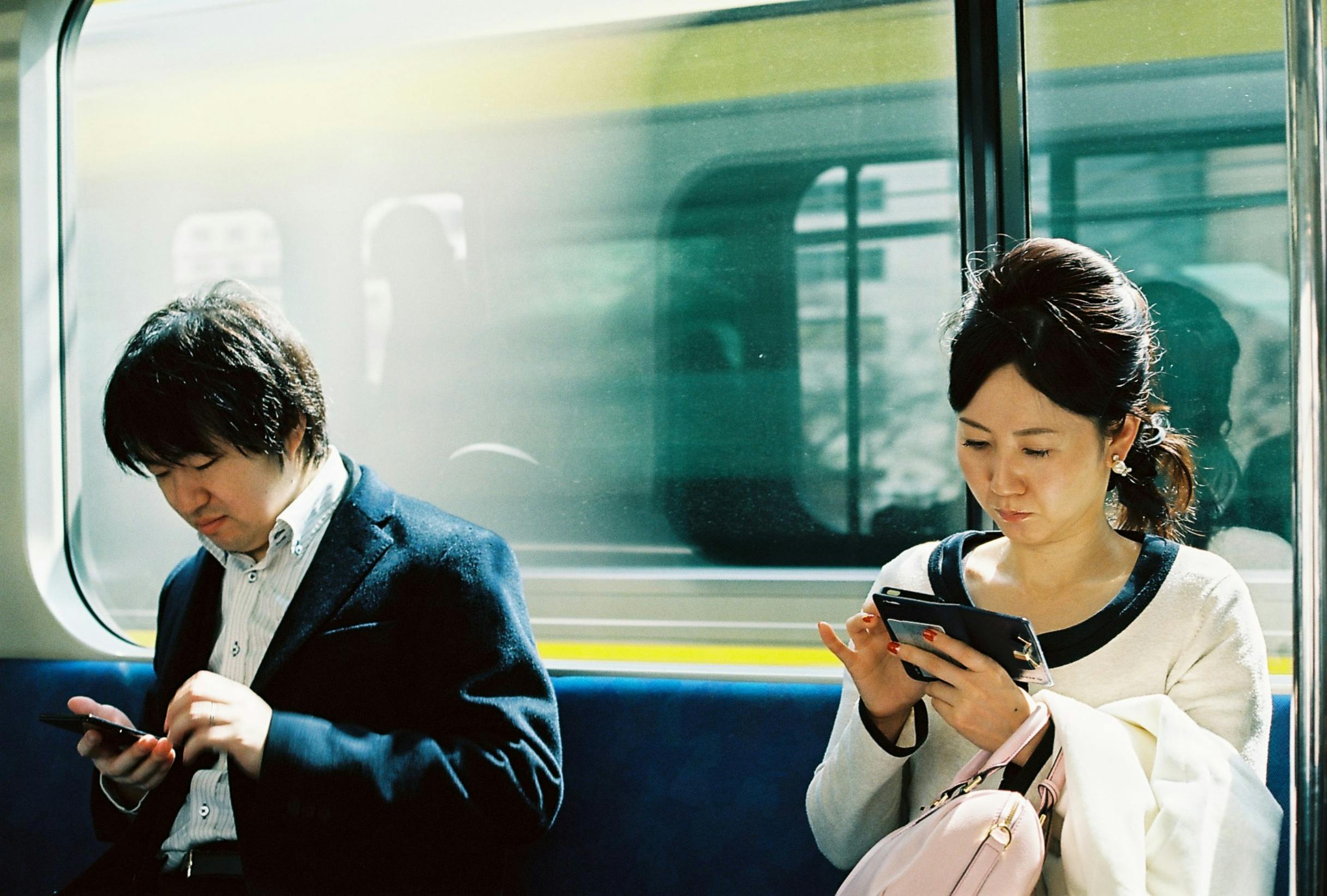 Two people using smartphones on a train in Tokyo, Japan. Captures daily commute and technology use.