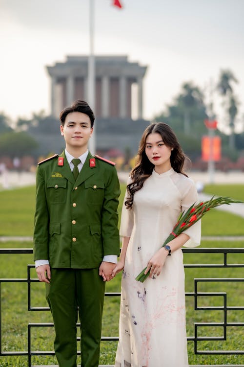A young couple in military uniforms standing in front of a flag