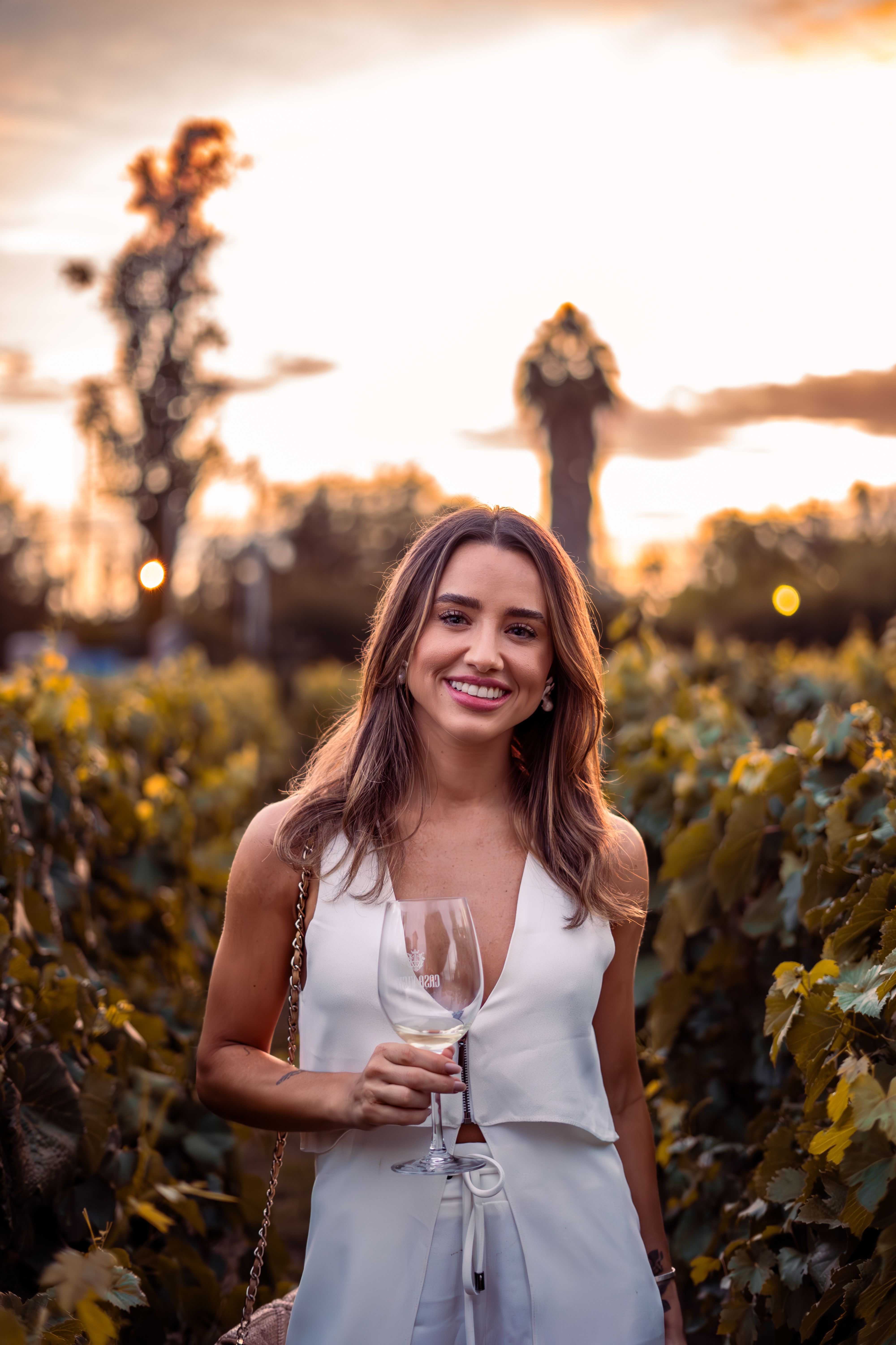 Caucasian woman in a vineyard enjoying a glass of wine during sunset.
