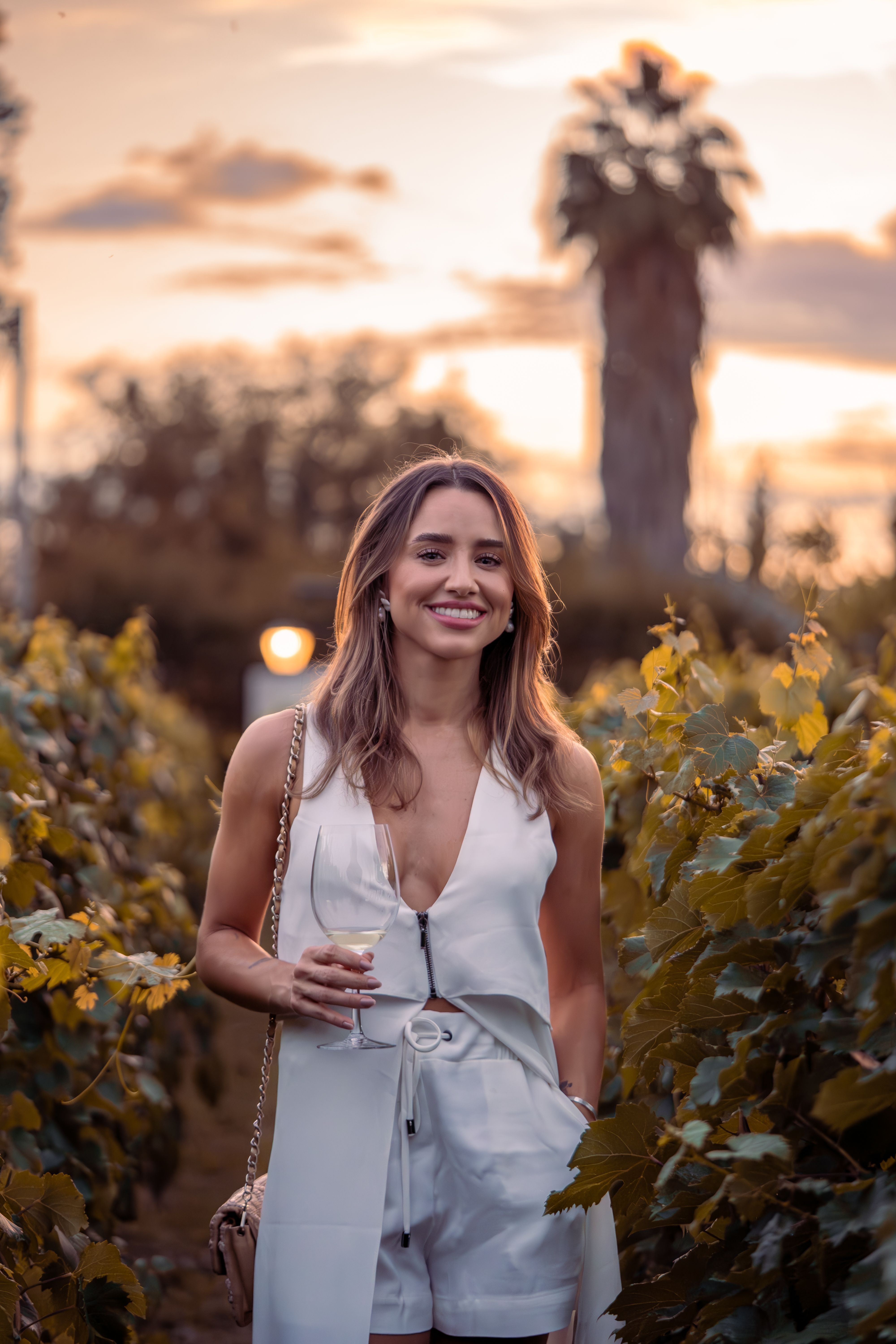 Woman in vineyard with wine glass at sunset, exuding a warm and inviting vibe.
