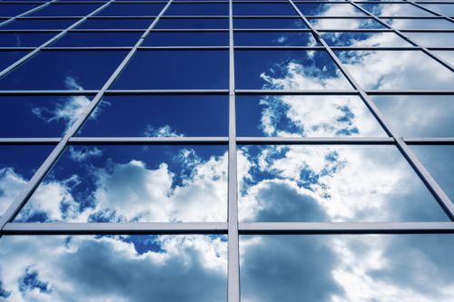Free Symmetrical glass facade of a modern building reflecting a bright, cloudy sky. Stock Photo