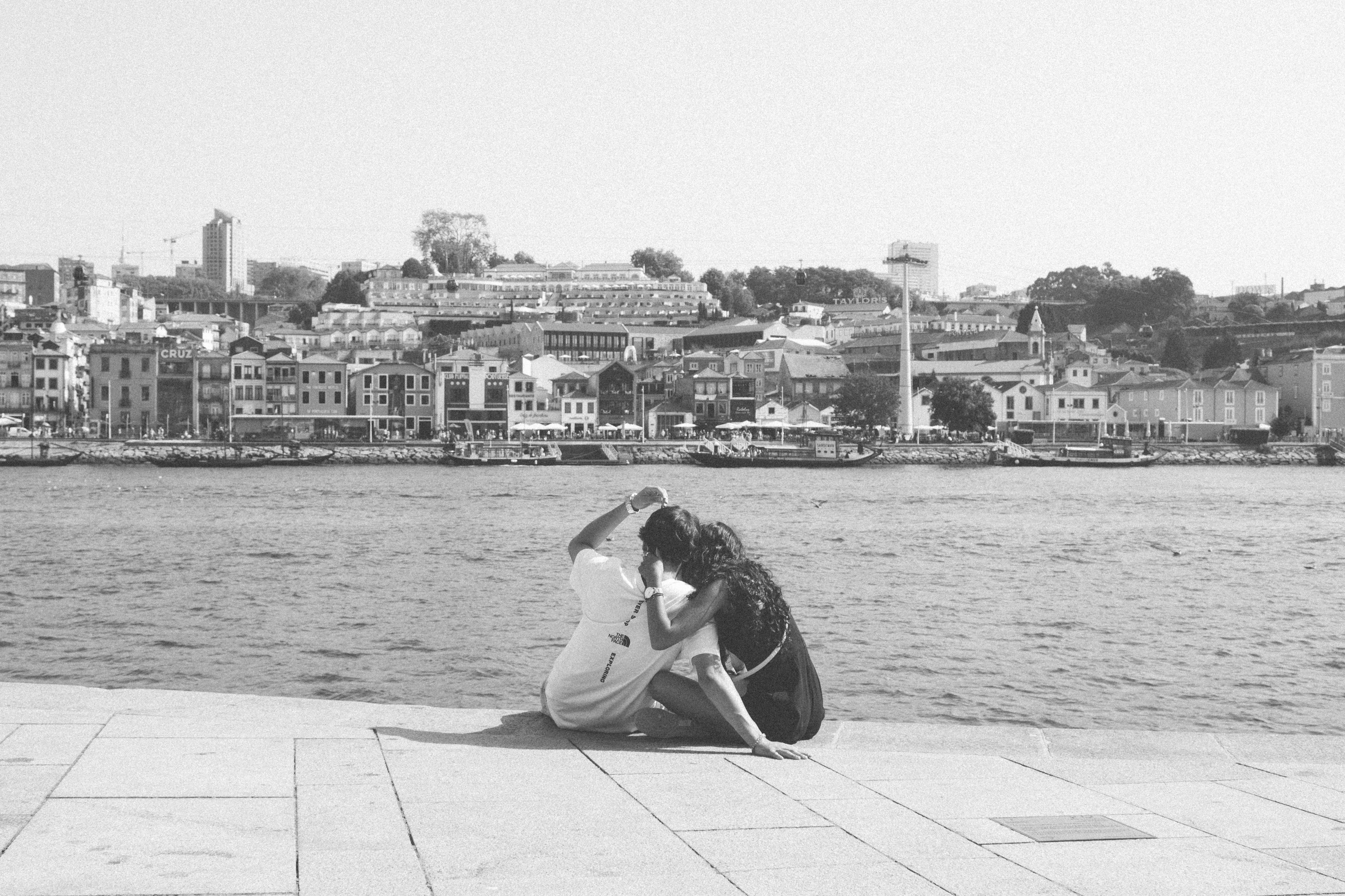 Couple sharing an intimate moment on the Porto riverfront with cityscape background.