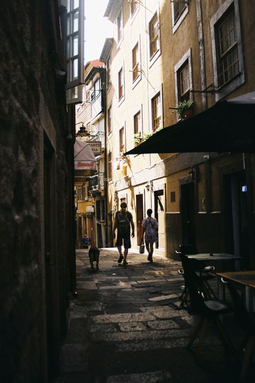 Free Sunlit narrow alley in Porto, Portugal with strolling pedestrians. Stock Photo