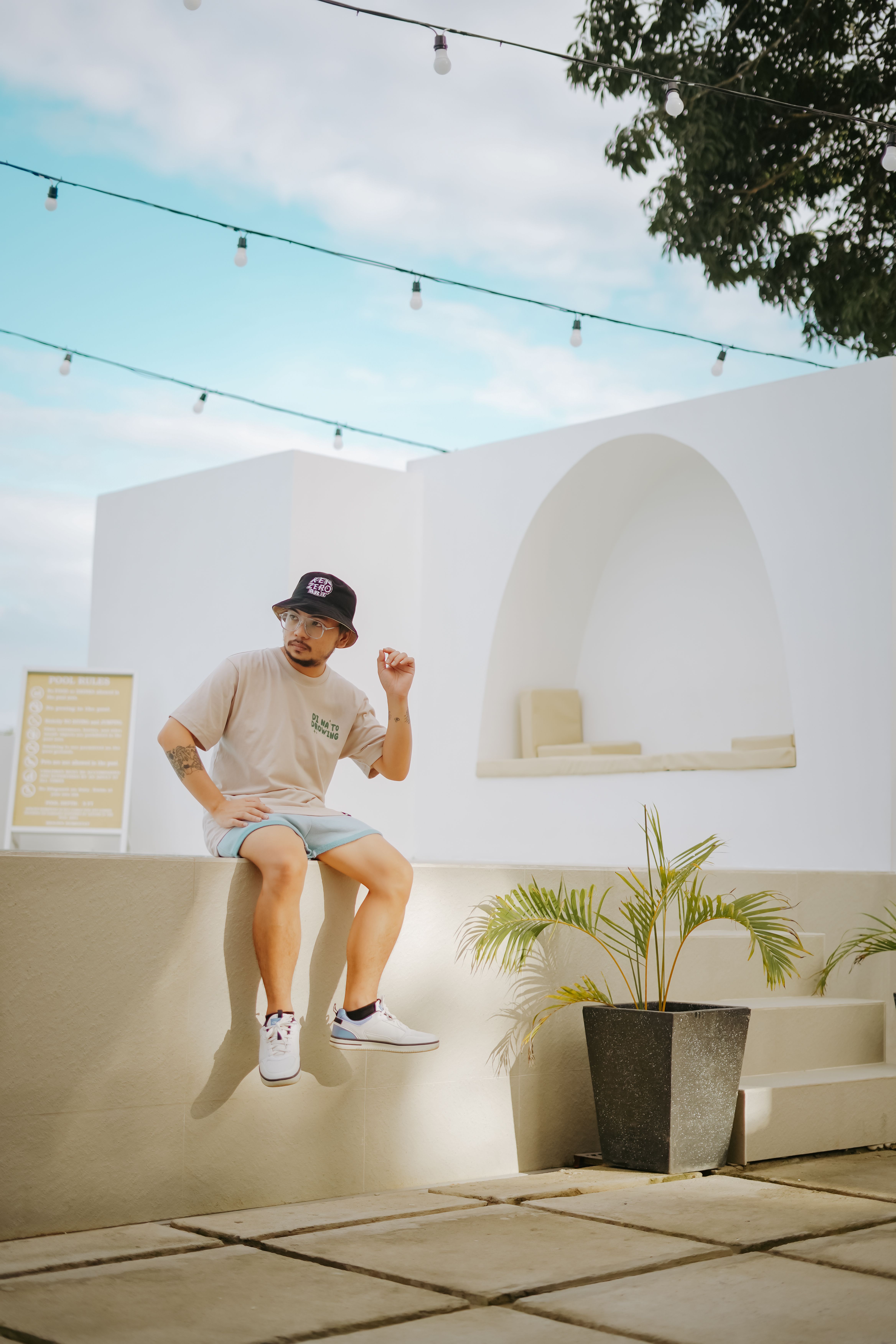 Man in casual attire sitting on a wall outside a modern building with plants.