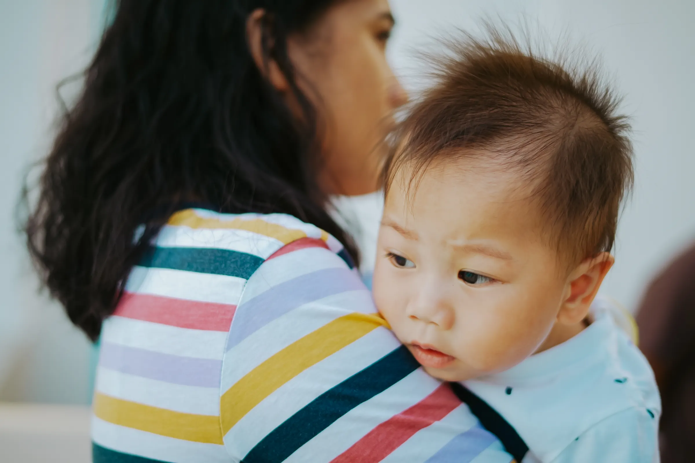 A mother holds her baby close indoors, sharing a quiet tender moment together