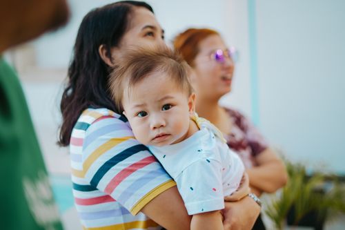 Free A mother affectionately holds her baby indoors, showcasing family warmth. Stock Photo