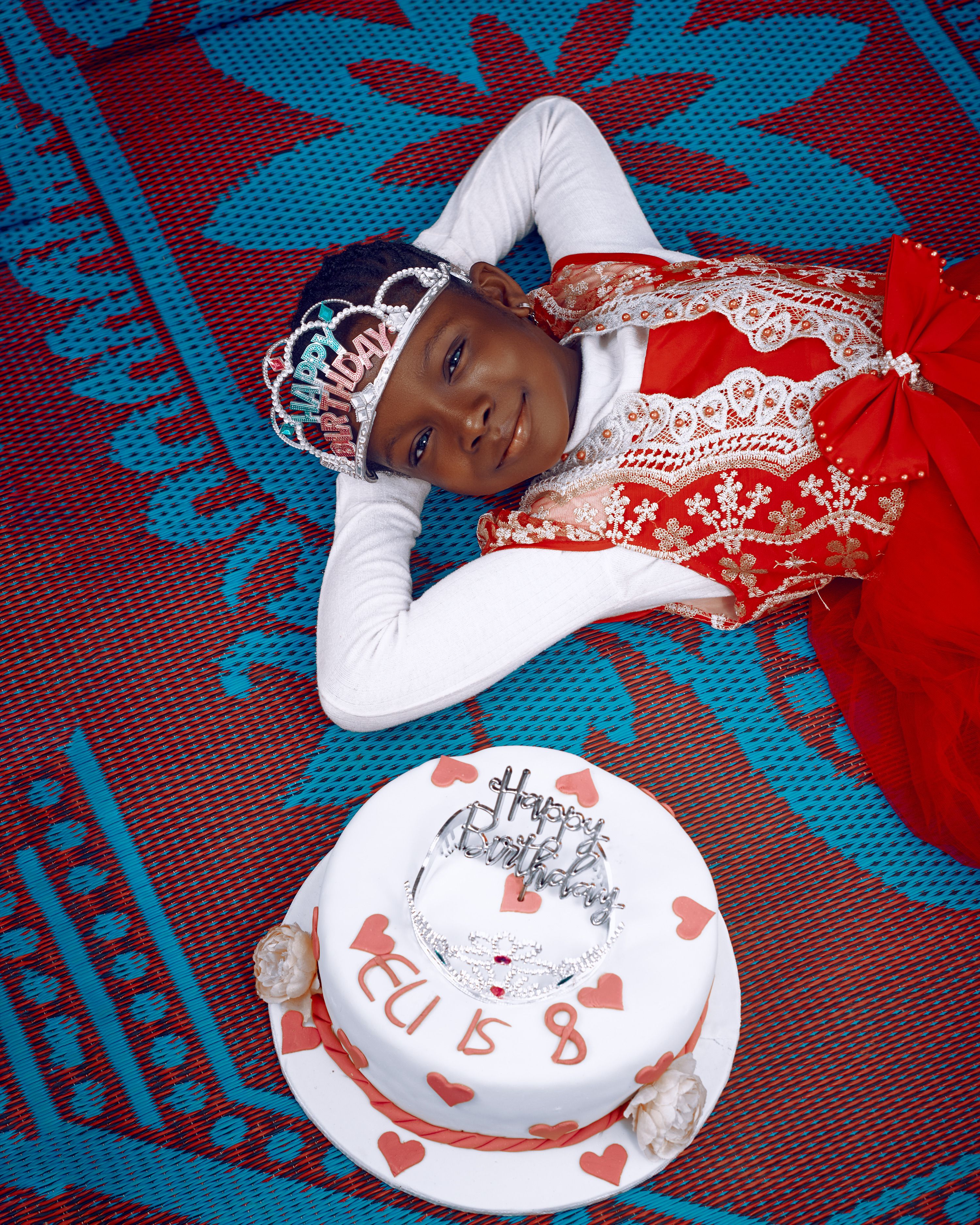 A joyful Nigerian girl in a festive dress celebrates her birthday with a decorated cake and crown.