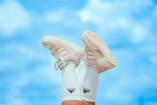 Free Legs wearing Adidas sneakers with white socks raised against a vivid blue sky. Stock Photo