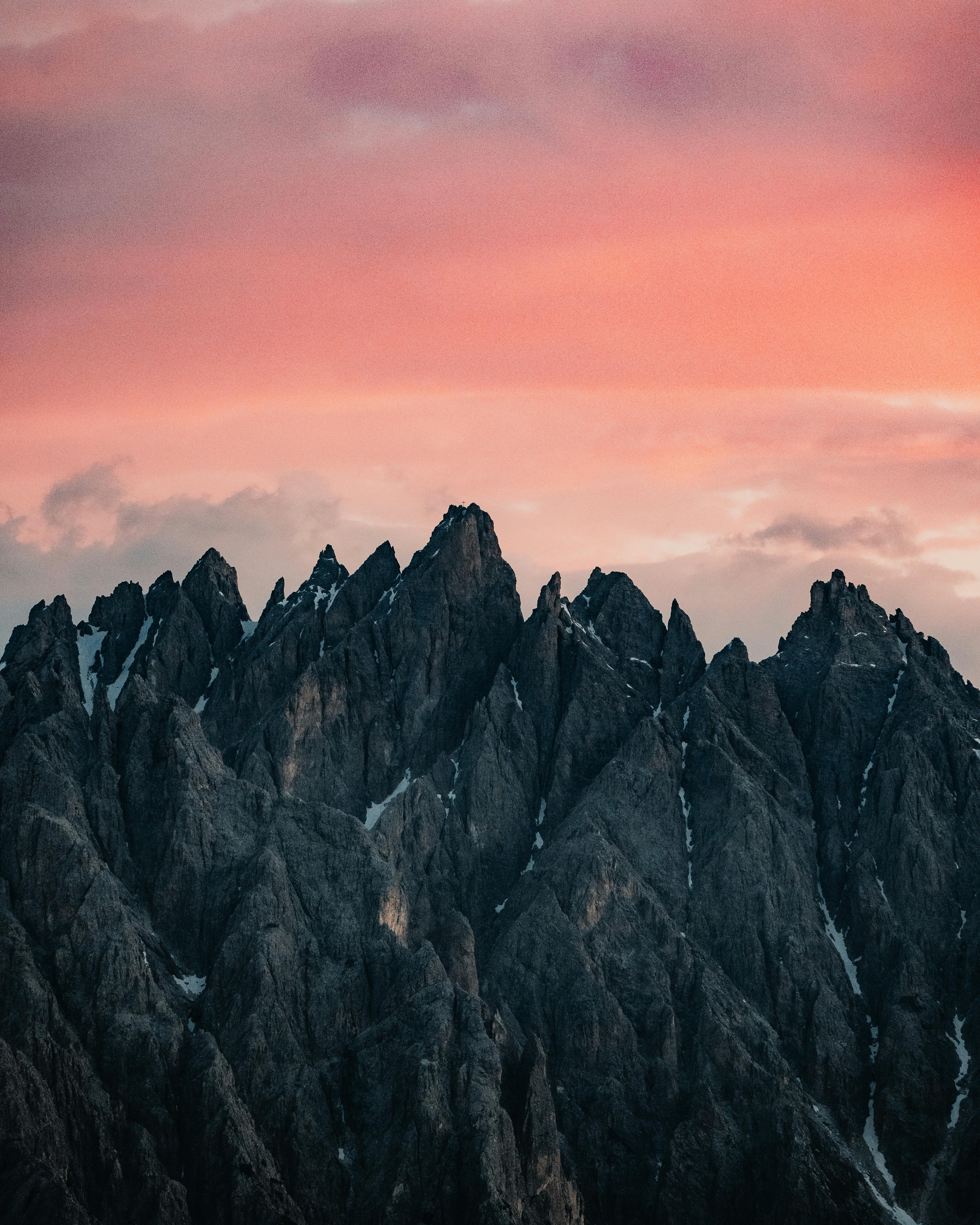 Dramatic rocky mountain peaks under a vibrant pink sky during sunset, Trentino-South Tyrol, Italy.