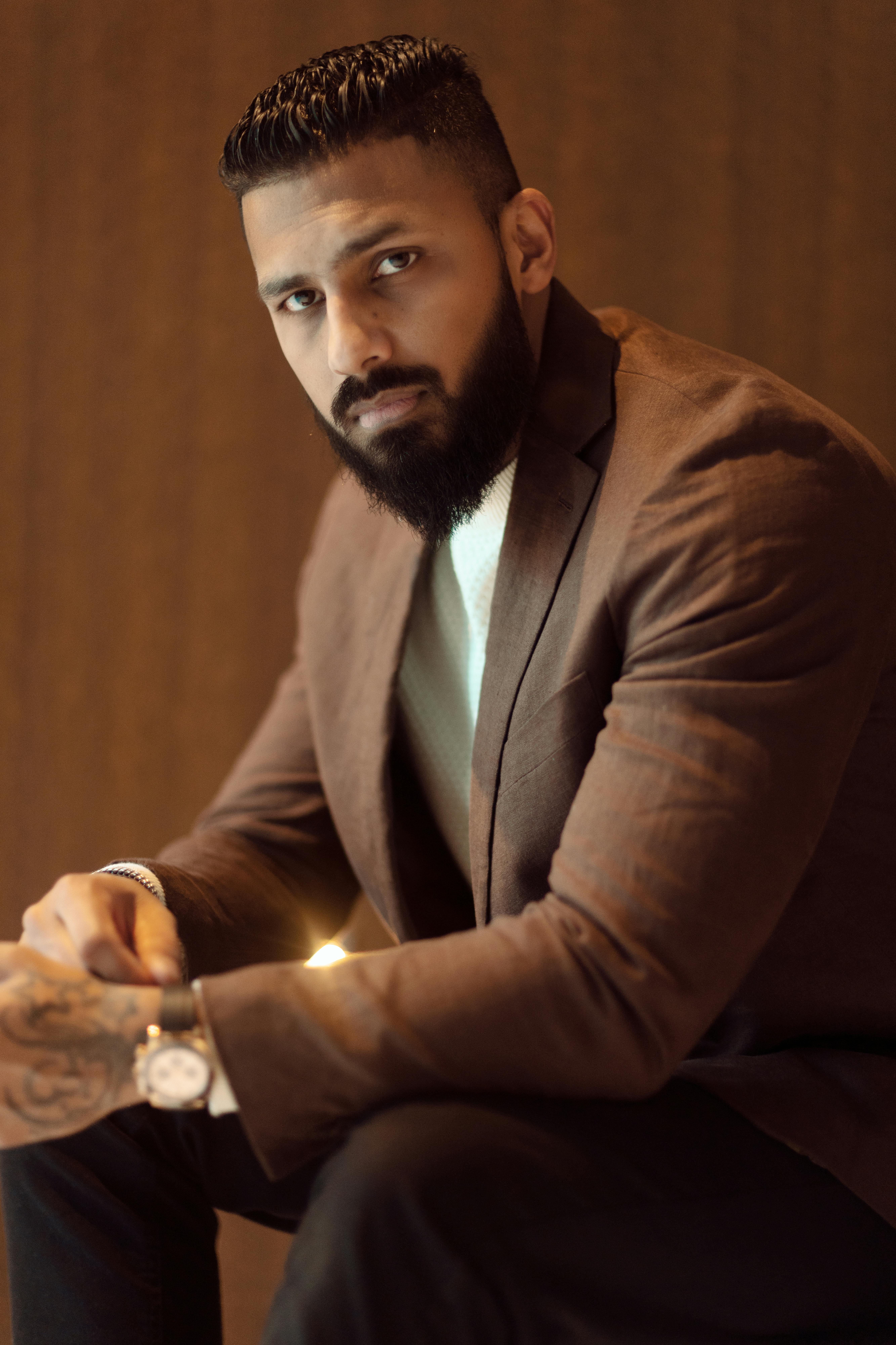 Portrait of a stylish bearded man in a brown blazer sitting indoors. Elegant and fashionable.
