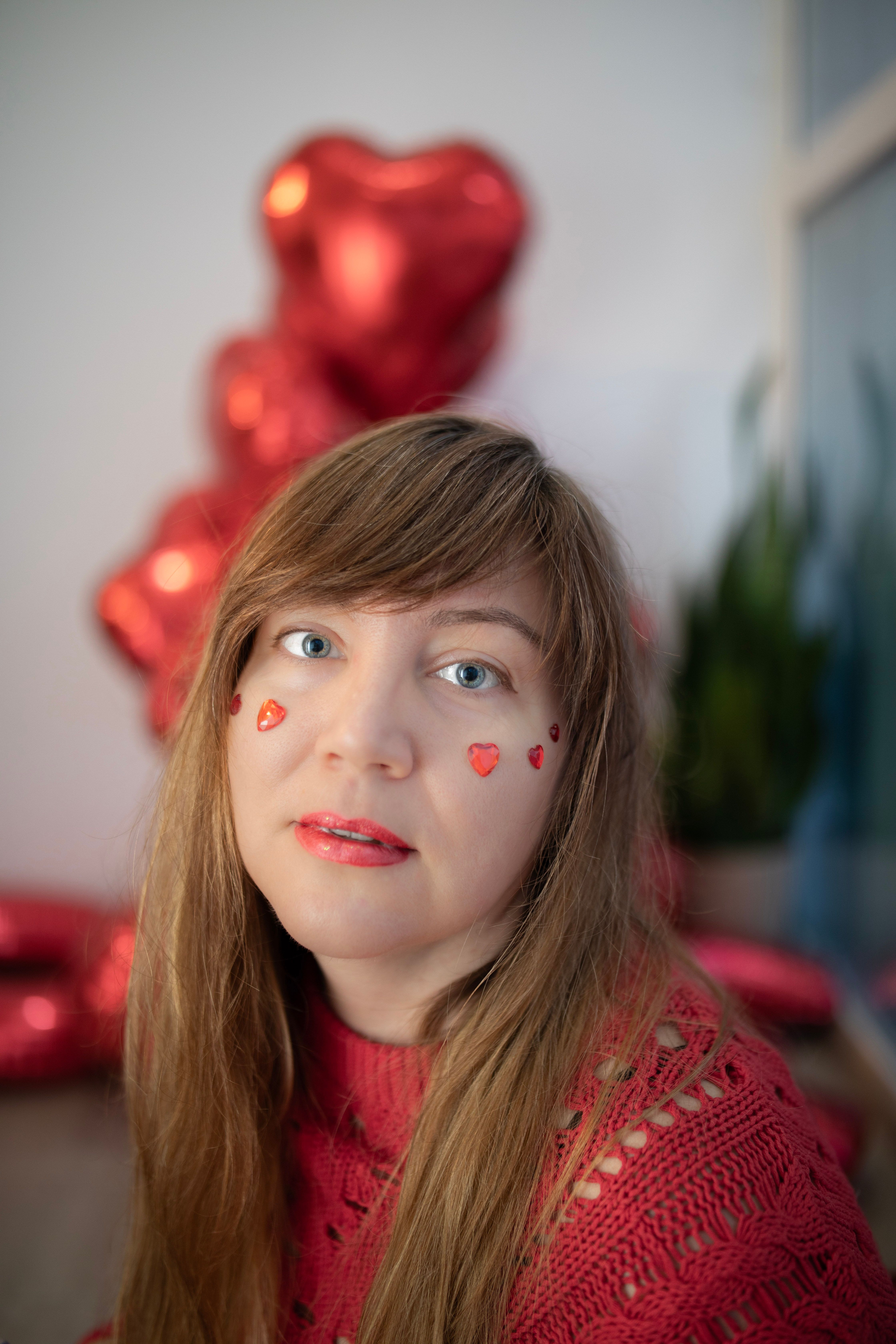 Portrait of a woman with heart stickers on her face and red balloons in the background.