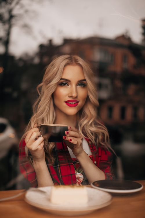 Free Charming blonde woman sipping coffee at a café, framed by a window backdrop. Stock Photo
