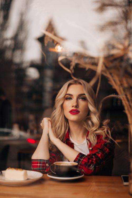 Free A fashionable blonde woman wearing red lipstick, sipping coffee in a chic café setting. Stock Photo