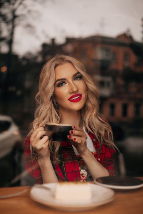Free Smiling blonde woman sipping coffee by a window in a cozy cafe setting. Stock Photo