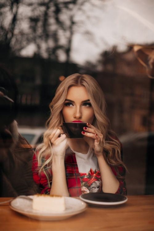 Free Stylish woman with long hair sipping coffee by a window in cozy café setting. Stock Photo