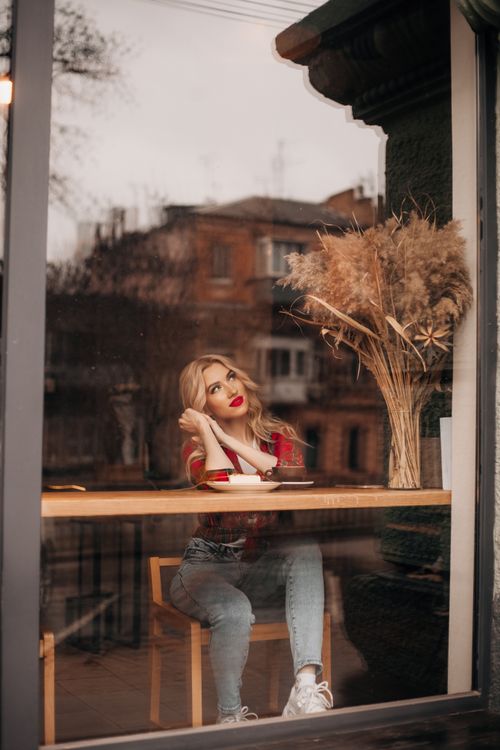 Free A thoughtful young woman with red lips, sitting by a cafe window, gazes outside while enjoying a tranquil moment. Stock Photo