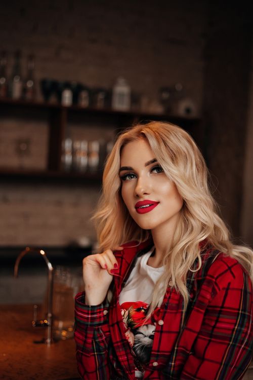 Free Stylish portrait of a blonde woman in a red checkered shirt, set in a warm indoor cafe environment. Stock Photo