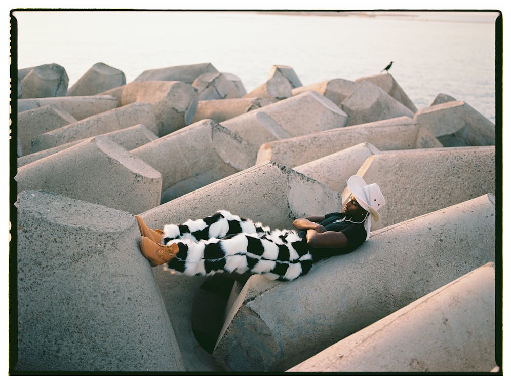 Man in Hat and Checkered Trousers Lying Down on Concrete Blocks