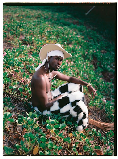 Topless Man in Hat and Checkered Trousers Sitting on Ground