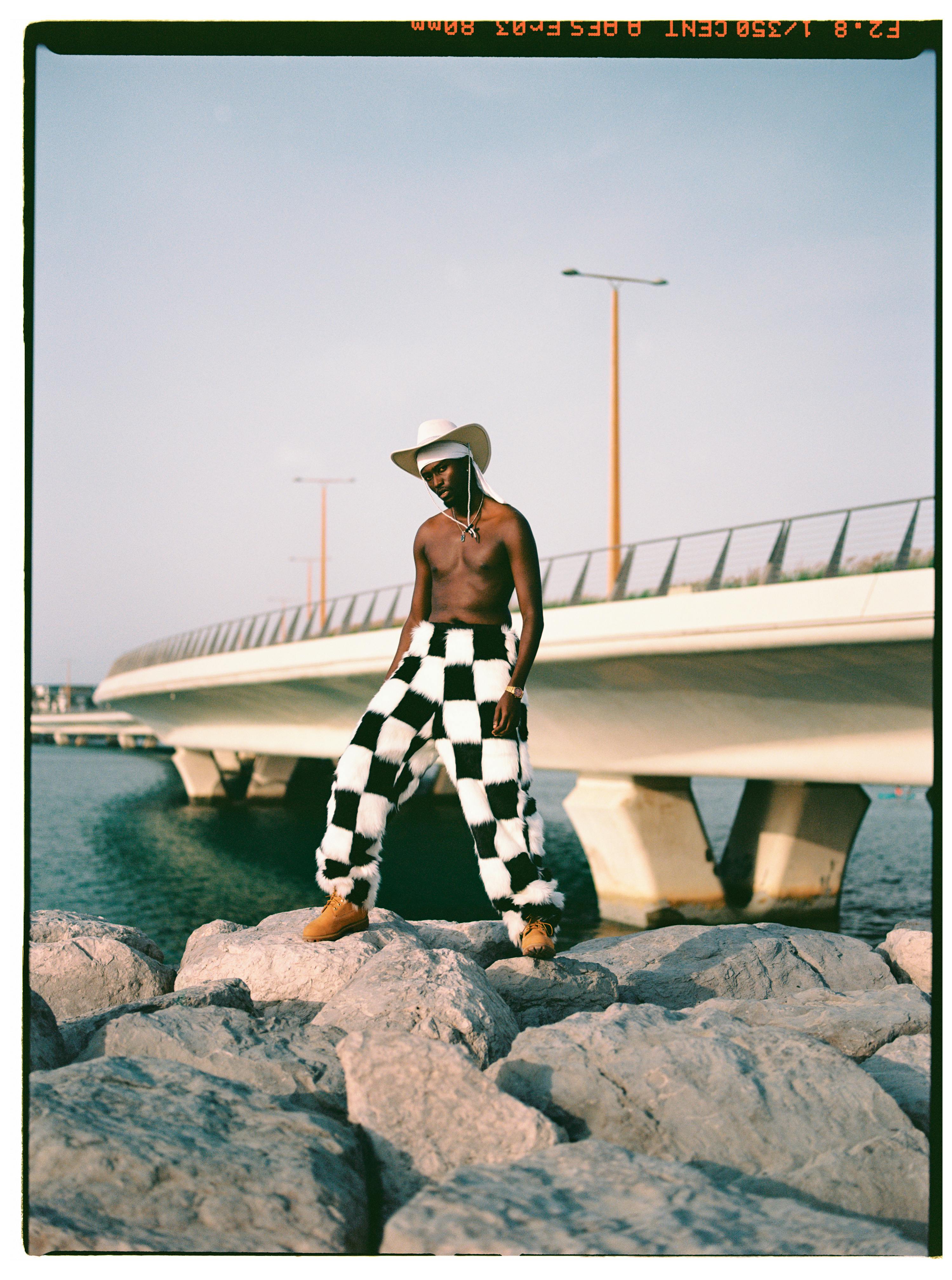 Bold fashion on display with a model posing by a contemporary bridge during sunset.