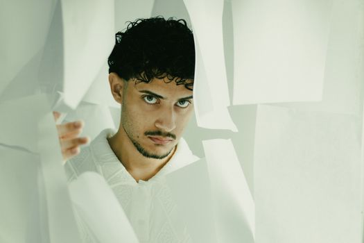 Expressive portrait of a man interacting with artistic paper sheets, conveying mystery and intrigue.