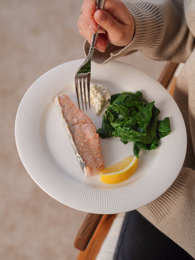 Close-up Of Woman Holding A Plate With Fish, Spinach And Lemon 