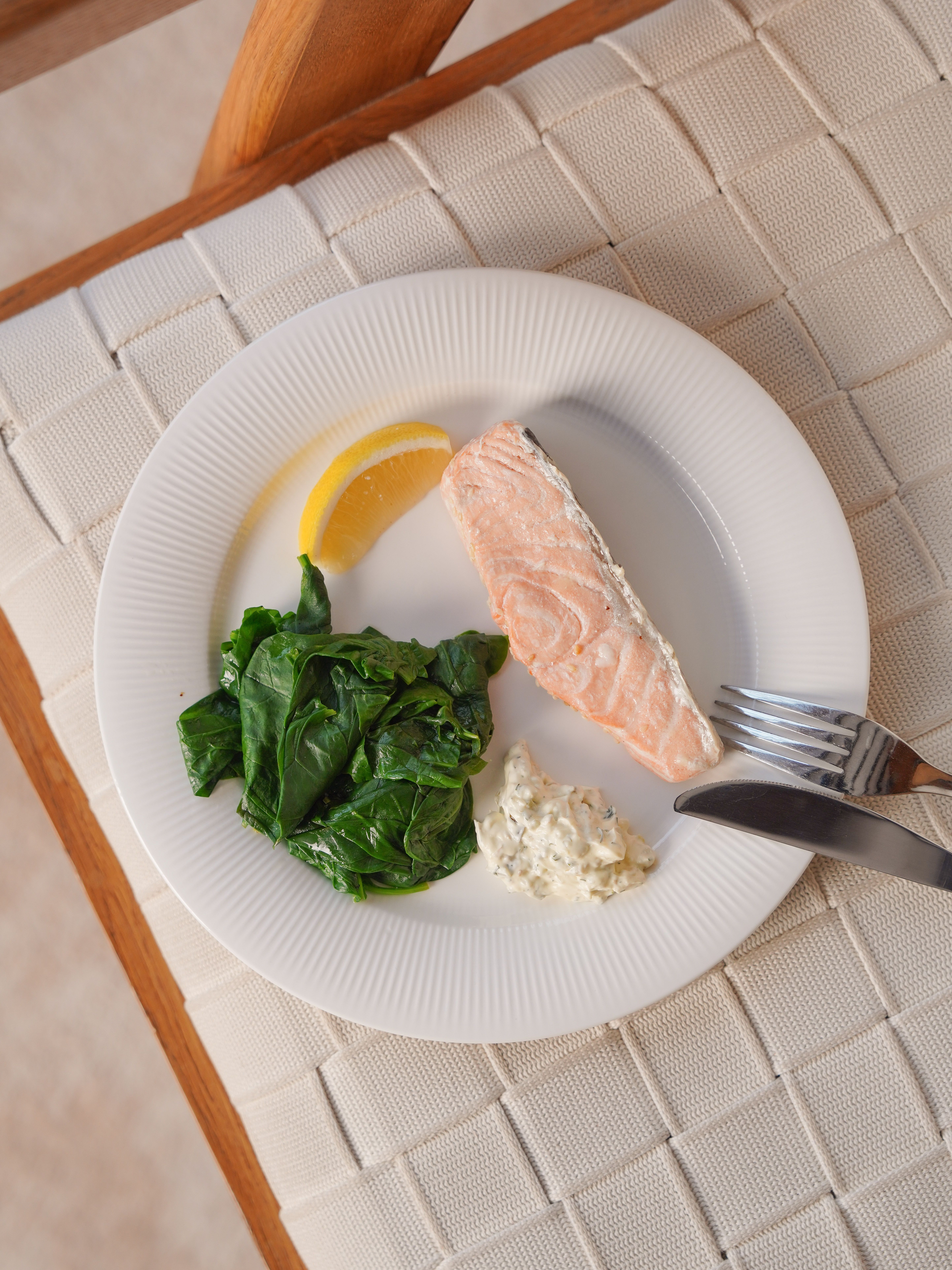 Delicious plate of salmon with sauteed spinach, lemon, and tartar sauce on a white plate.