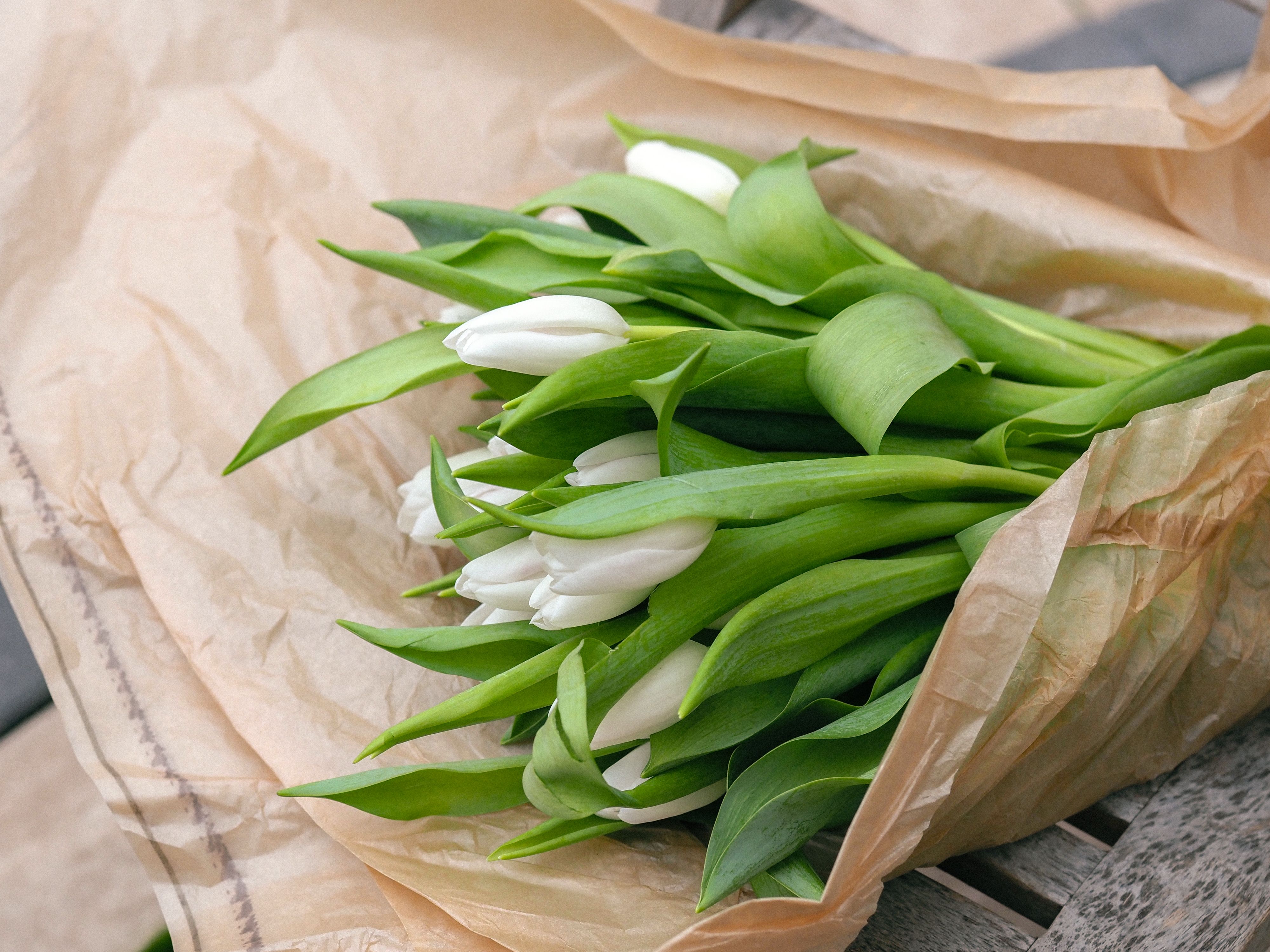 A hand-tied bouquet wrapped in kraft paper resting on a linen cloth.