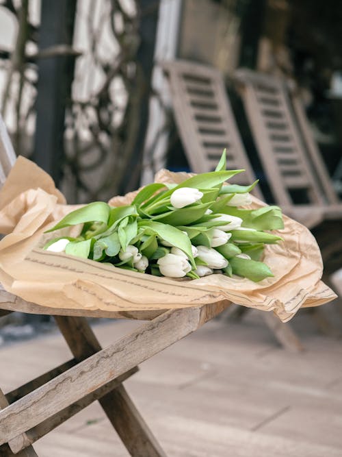 A bouquet of white tulips sitting on a wooden chair