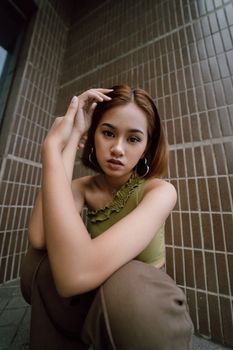 Stylish young woman in casual attire poses in front of a modern brick wall, embodying urban fashion trends.