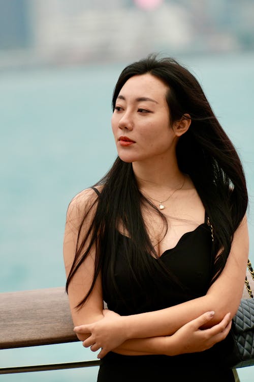 A woman in a black dress standing near a body of water