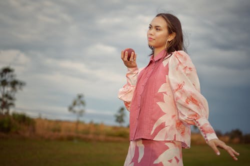 A woman in a pink and white dress is holding an apple