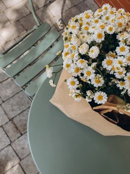 A brown paper bag holds daisies on a green table, evoking romantic spring vibes.