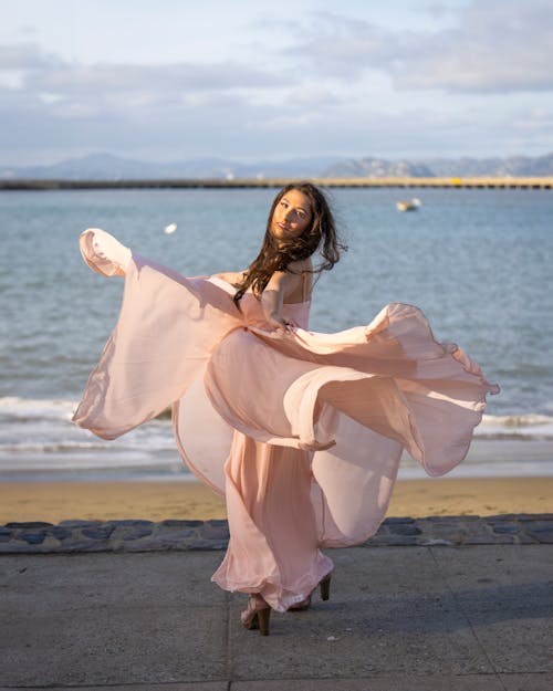 Young Woman in a Pink Dress Dancing on a Shore 