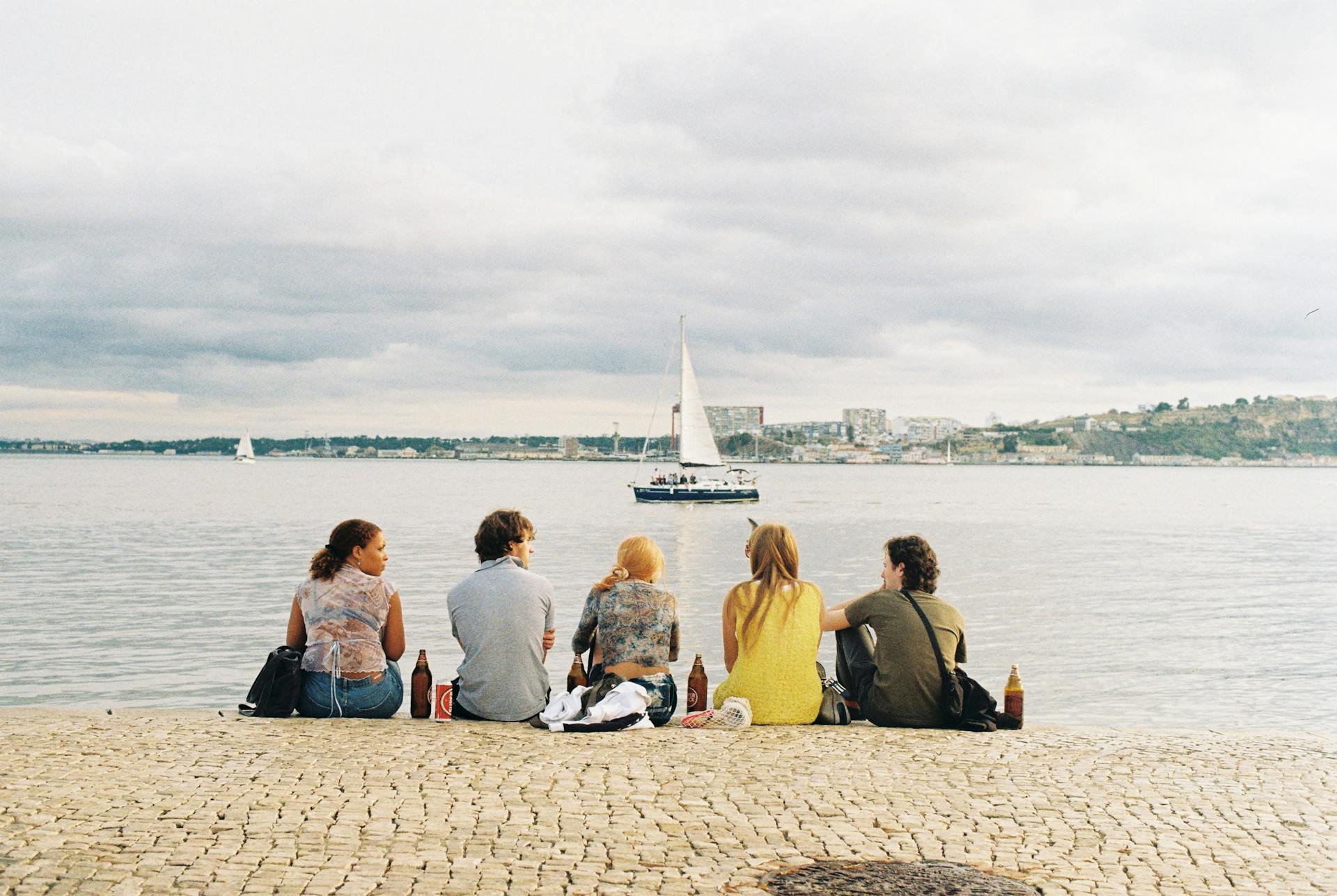 Group of friends enjoying a scenic view by the Lisbon waterfront on a cloudy day.