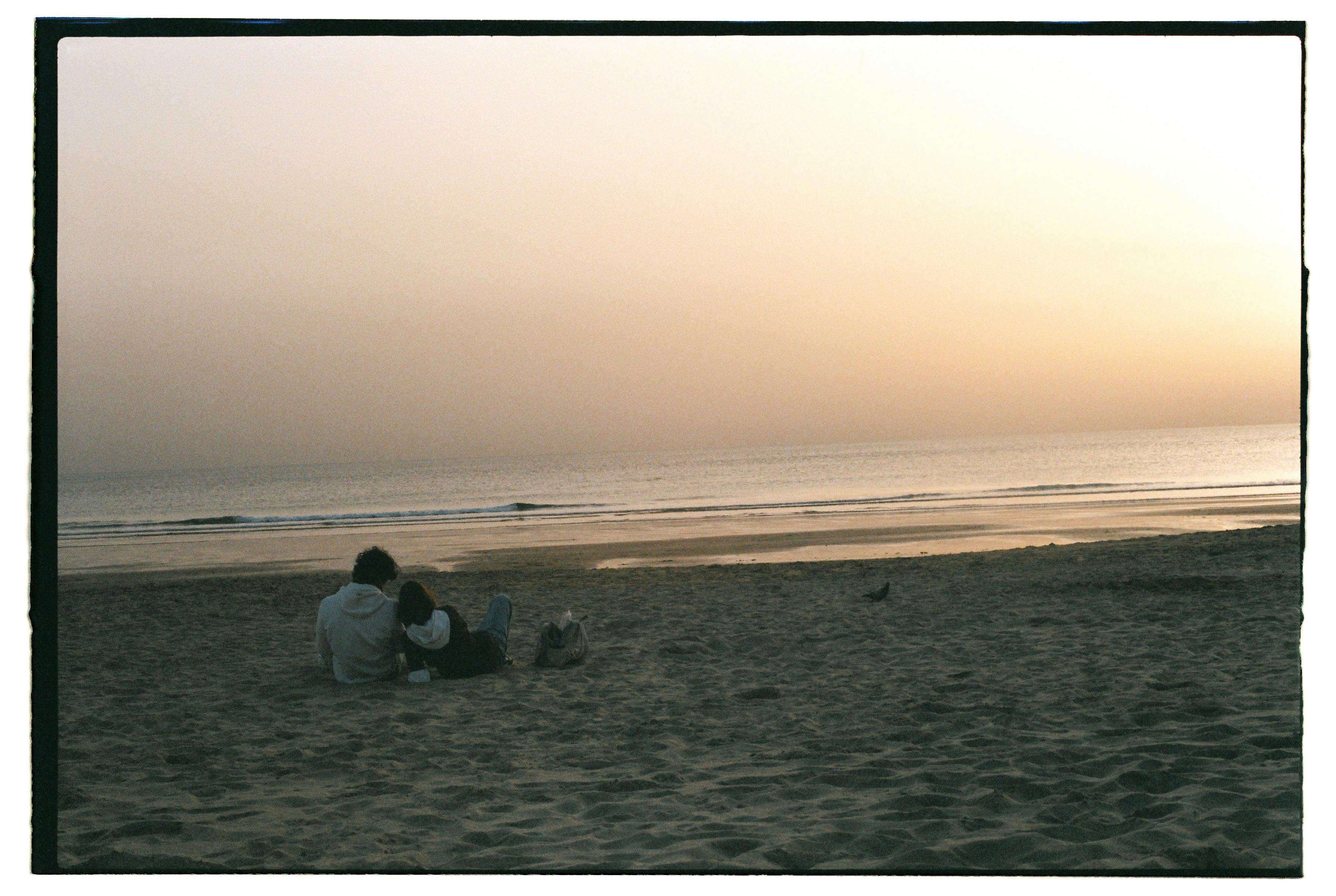 A couple enjoying a serene sunset on a sandy Lisbon beach.