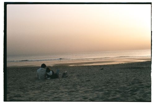 Free A couple enjoying a serene sunset on a sandy Lisbon beach. Stock Photo