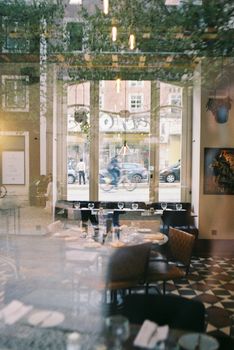 Cozy Lisbon restaurant interior with window reflections of city life on a bright day.