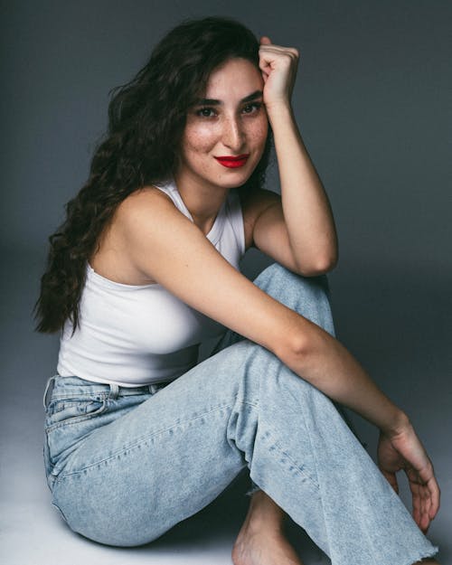 A woman in jeans and white top sitting on the floor