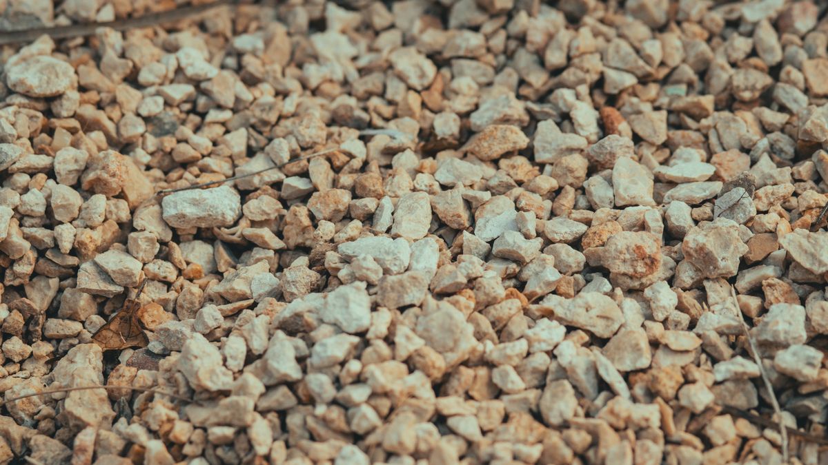 Close-up of beige gravel. Rounded stone packs differently from crushed stone, so the same ton fills a different volume.