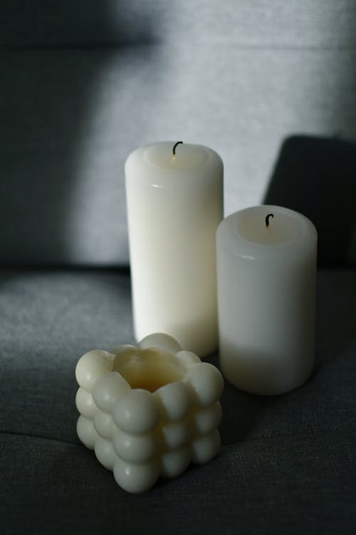 Two white candles sit on a table next to a cube