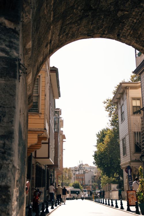 Free Historic urban street view framed by a stone archway, featuring classic architecture and vibrant city life. Stock Photo