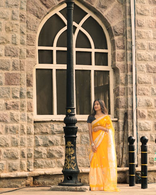 A woman in a yellow sari standing next to a lamp post
