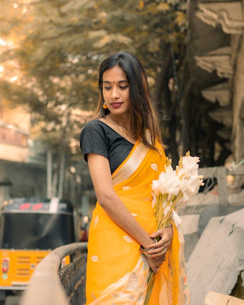 A woman in a yellow sari holding flowers